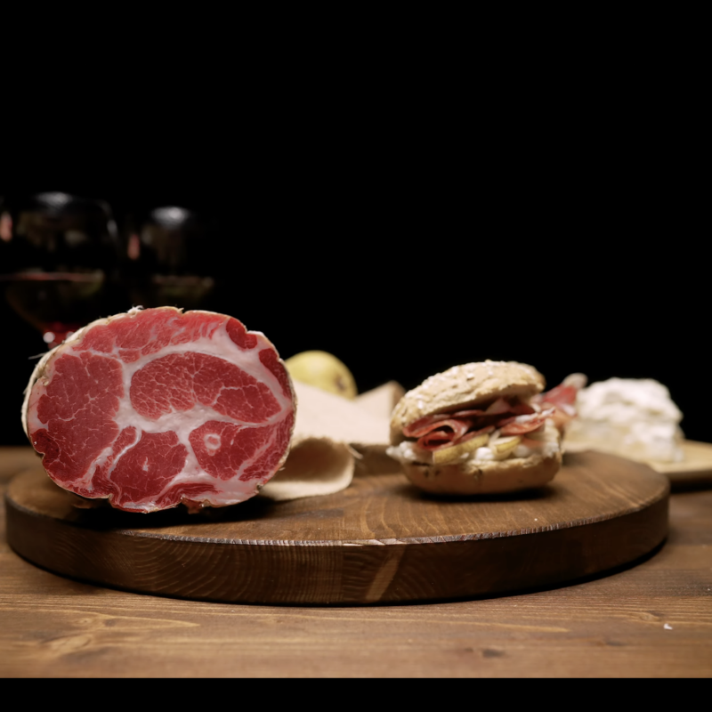 Salumi Pasini coppa packshot with bread roll, pear, cheese and red wine glass on wooden rotating board — TV commercial food photography by Uptelling, Milan Italy