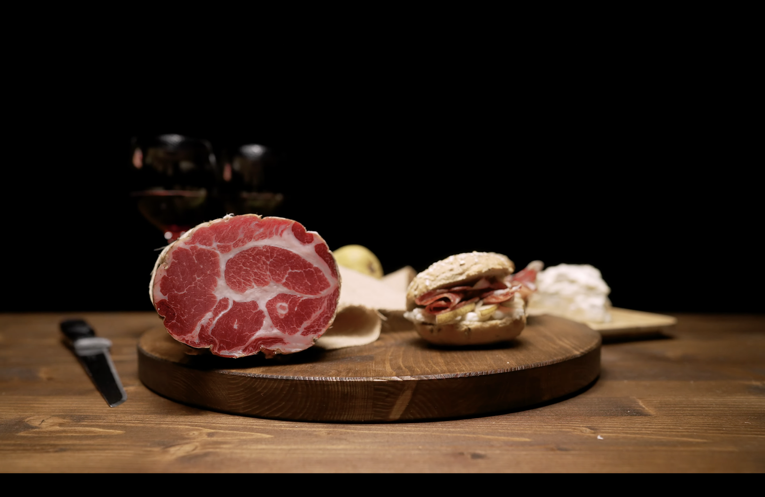 Salumi Pasini coppa packshot with bread roll, pear, cheese and red wine glass on wooden rotating board — TV commercial food photography by Uptelling, Milan Italy