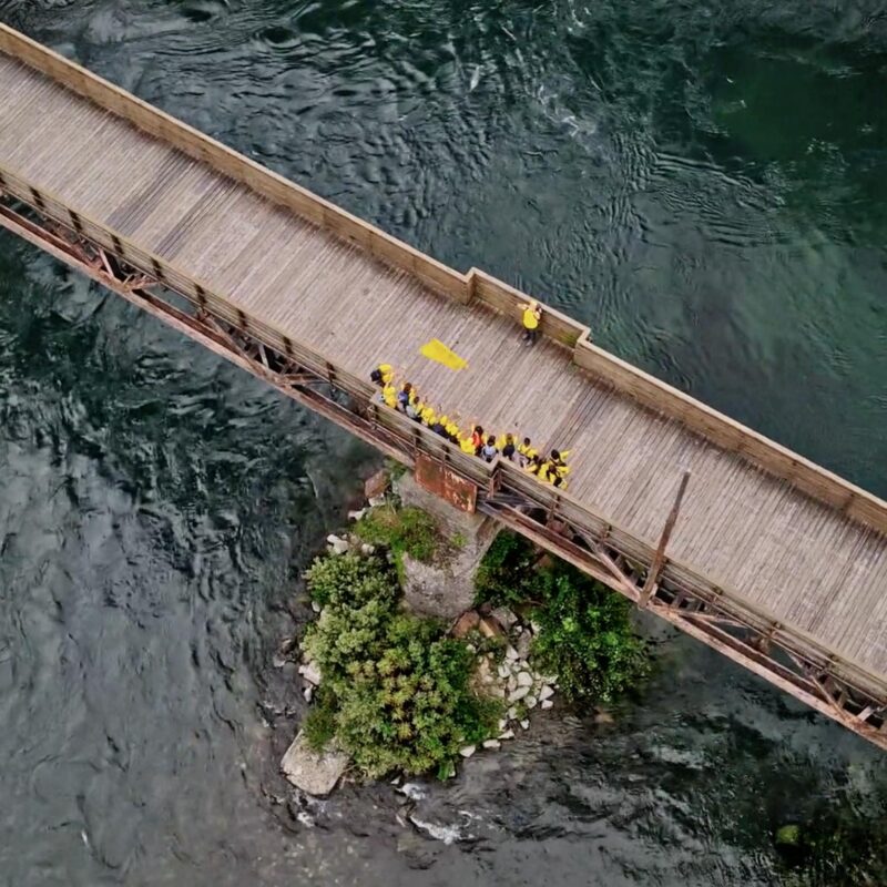 Aerial drone shot of visually impaired teenagers crossing wooden bridge over flooded river on Cammino di Leonardo — Noisy Vision documentary by Uptelling, Lecco to Milan inclusive walk 2021